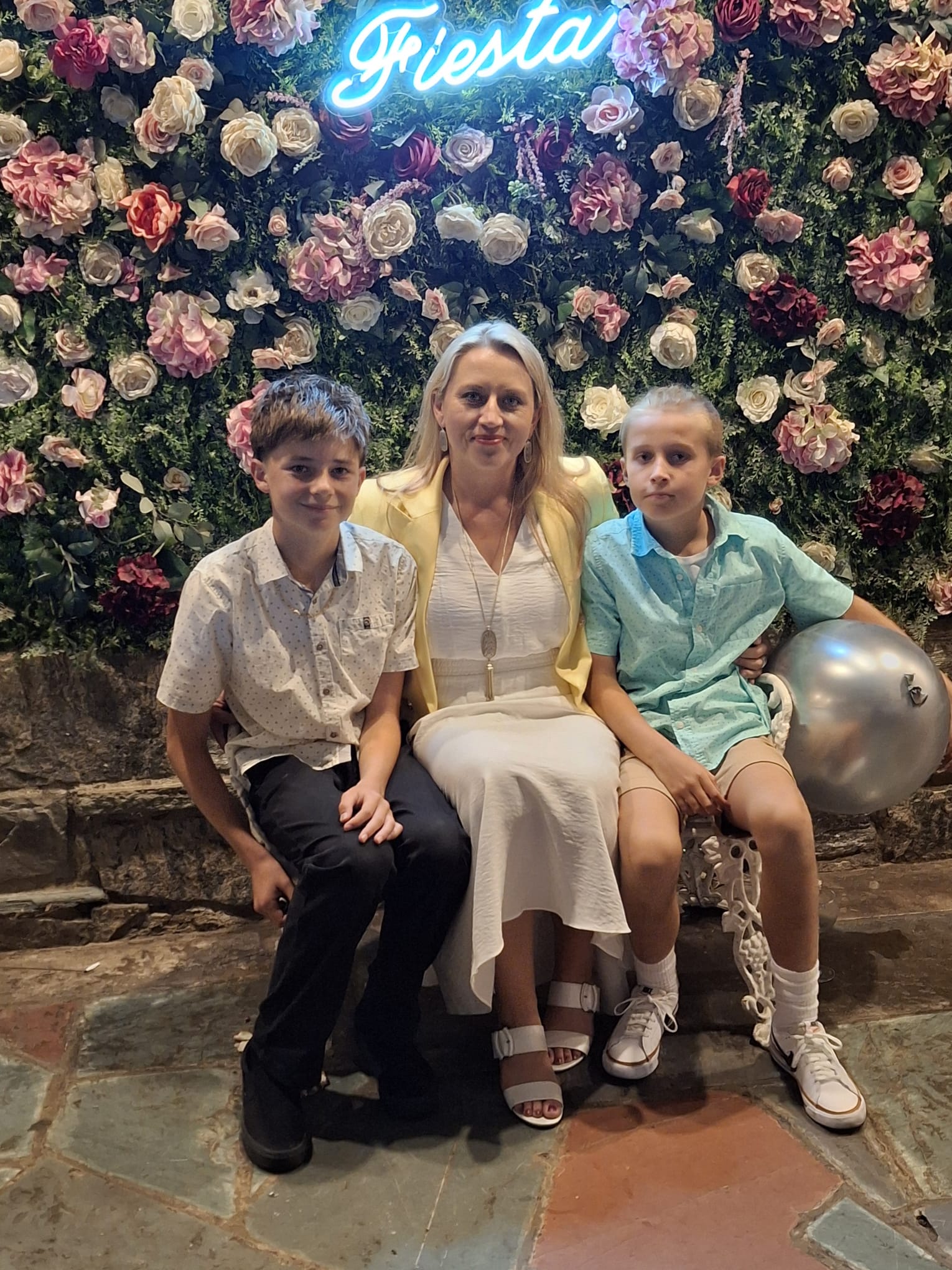 Pearl sitting with her two sons in front of a flower wall.