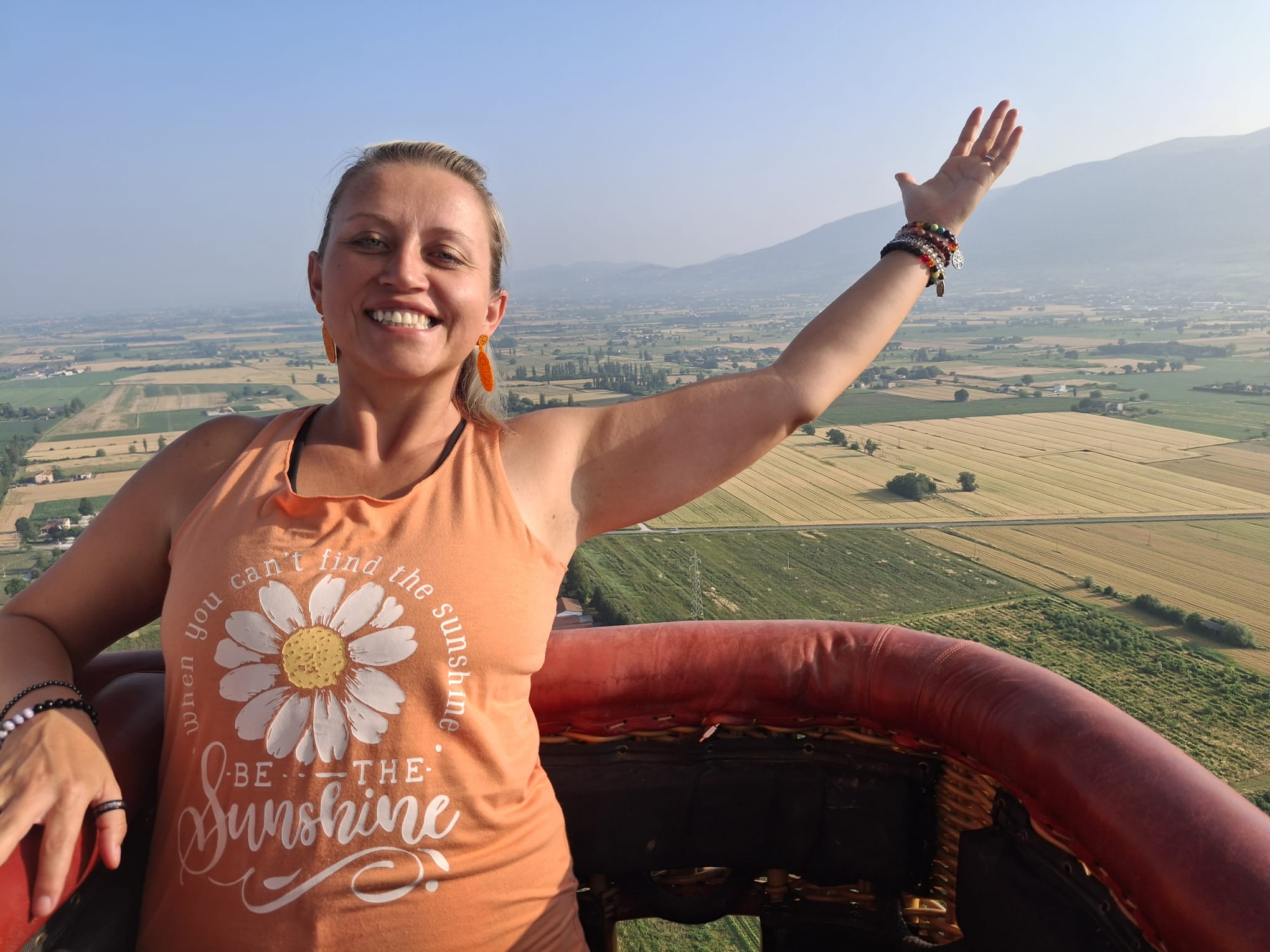Pearl smiling with her arm raised above a wide landscape.